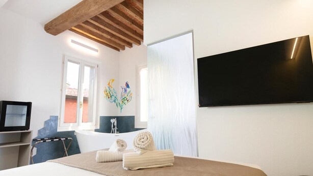 A hotel room with a bed, a TV, a bathtub, and a wall-mounted TV.