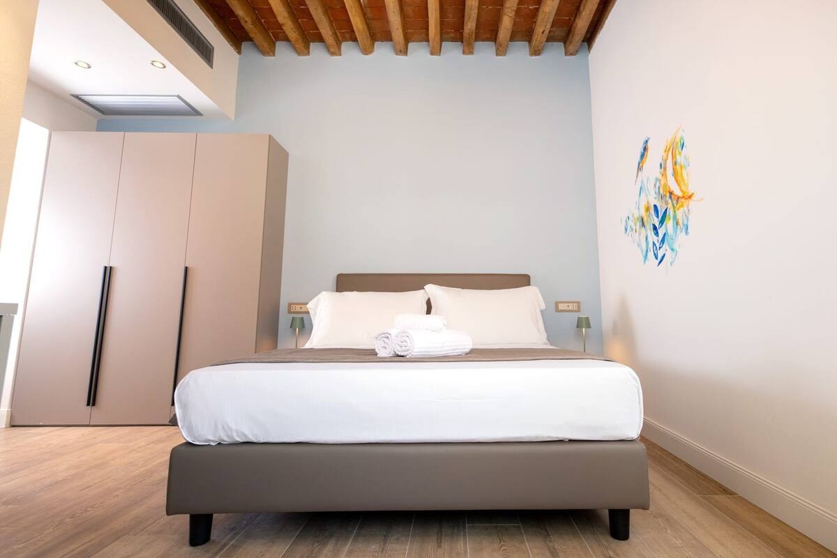 Un dormitorio con cama, armario, un cuadro y techo con vigas de madera.
