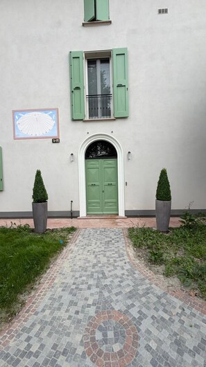 Fachada de edificio con puerta verde, un reloj y dos macetas.