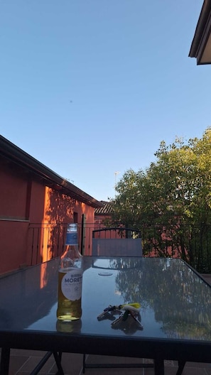 A glass table with a bottle of liquor and keys on it, set against a clear sky and a building with a red facade.