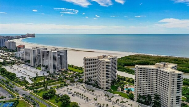 Um hotel à beira-mar com vários edifícios altos, uma praia e um estacionamento.
