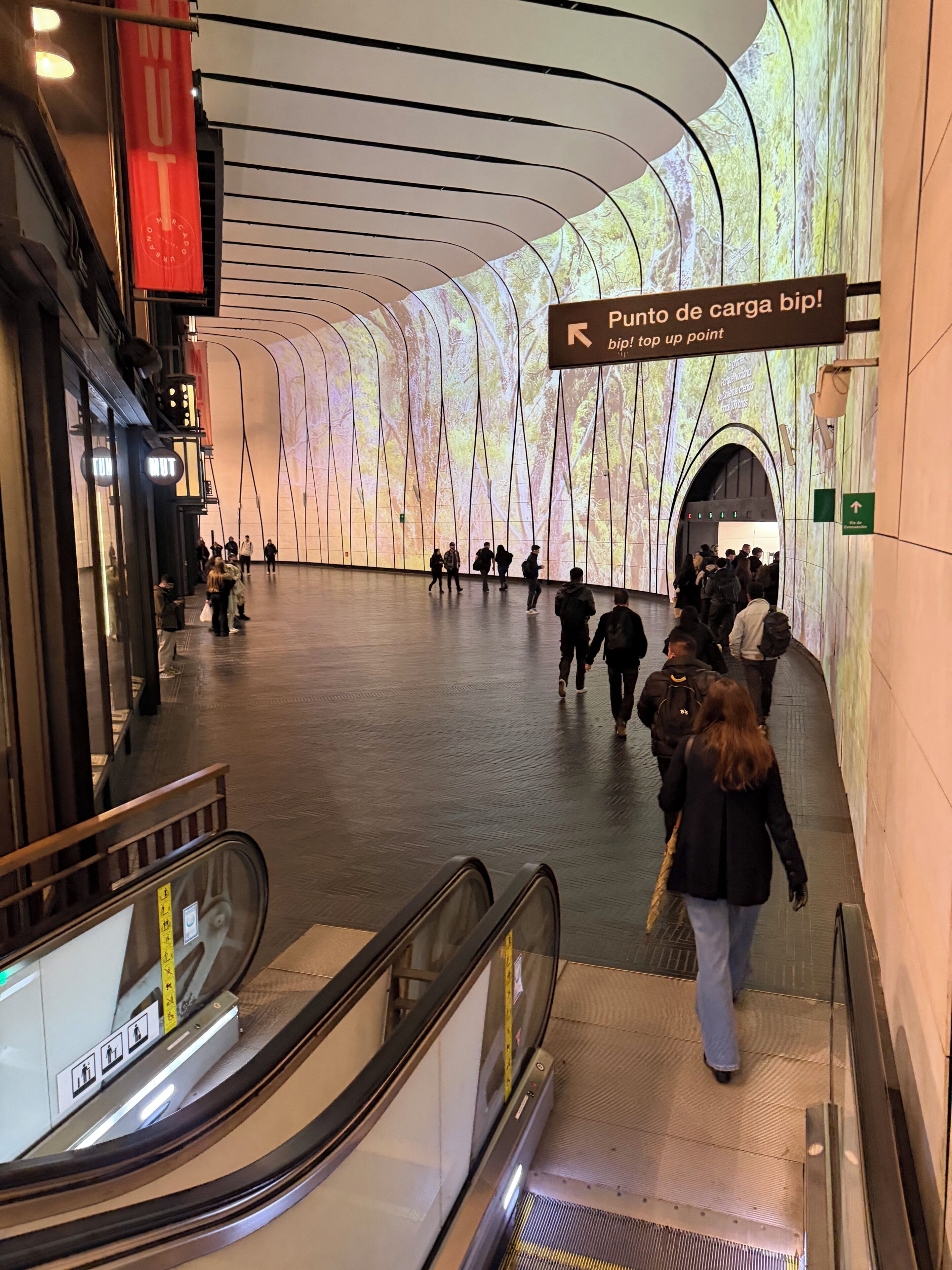 An indoor public space with a modern architectural design, including a curved ceiling and a large digital display.