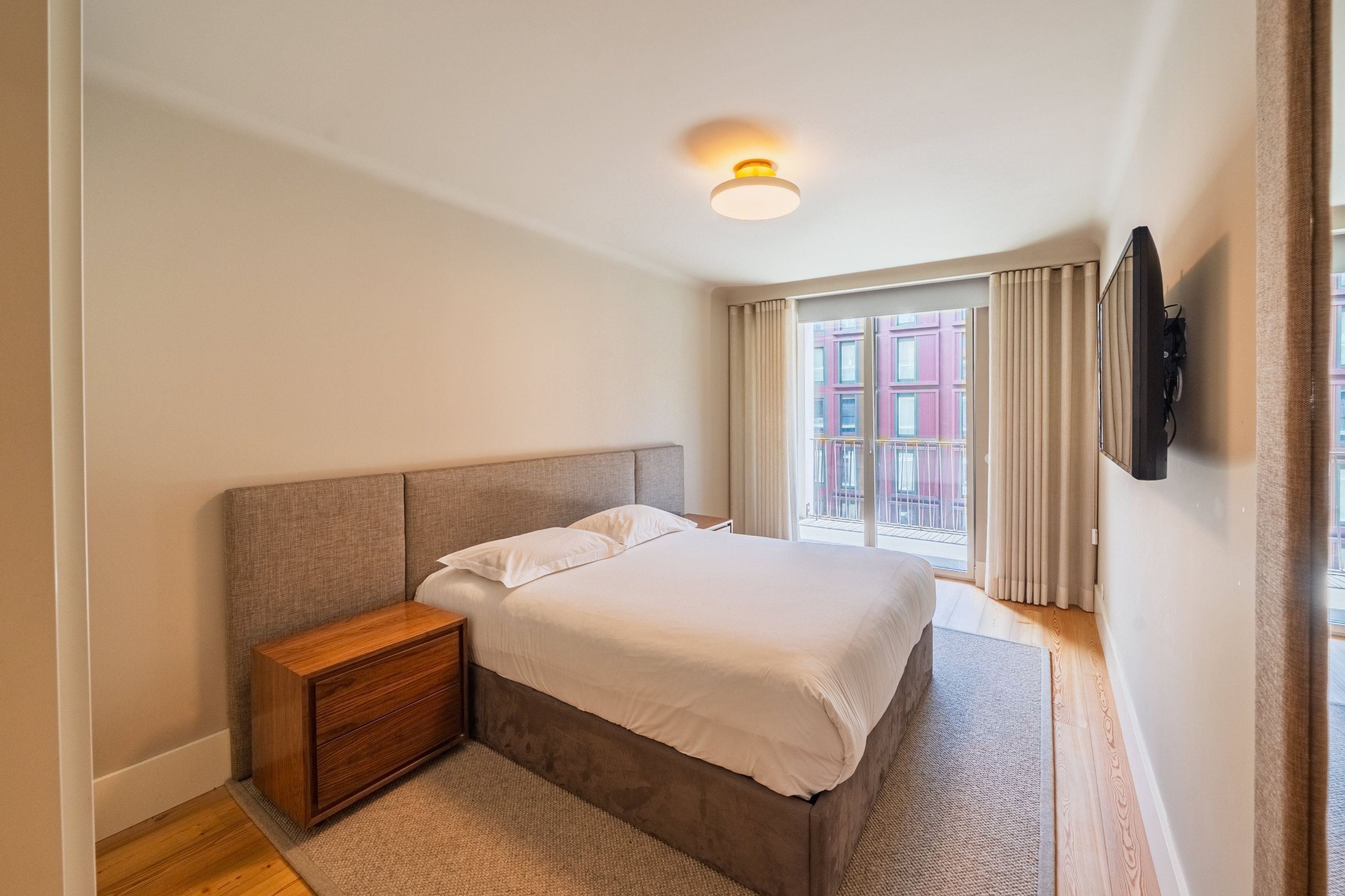 A bedroom with a bed, nightstand, and a television mounted on the wall.