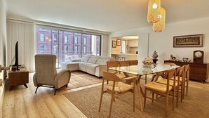 A modern living room with a glass dining table, wooden chairs, a sofa, and a large window overlooking a building. - Z - Market Residence 1D (Porto)