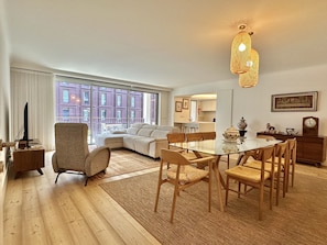 A modern living room with a glass dining table, wooden chairs, a sofa, and a large window overlooking a building. - Z - Market Residence 1D (Porto)
