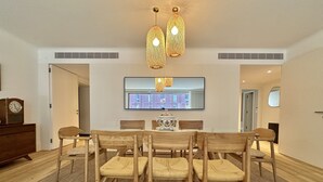 A dining area with a round table, six chairs, two hanging lights, a clock, and a television on the wall. - Z - Market Residence 1D (Porto)