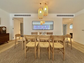 A dining area with a round table, six chairs, two hanging lights, a clock, and a television on the wall. - Z - Market Residence 1D (Porto)