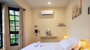 A hotel room with a bed, bedside lamp, air conditioning unit, and a window with curtains.