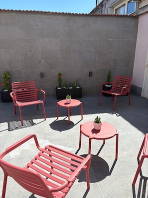 Um espaço de pátio com cadeiras e mesas de metal vermelho, plantas em vasos e uma parede revestida com azulejos.