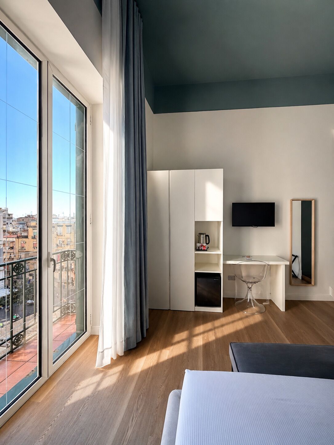 A modern hotel room with a balcony, a desk, a bed, and a TV.