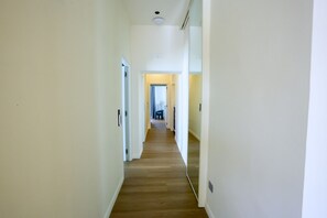 A narrow hallway with wooden flooring and white walls, leading to a room with a bed and a window. - Altanapoli Rooms & Suites (Napoli)