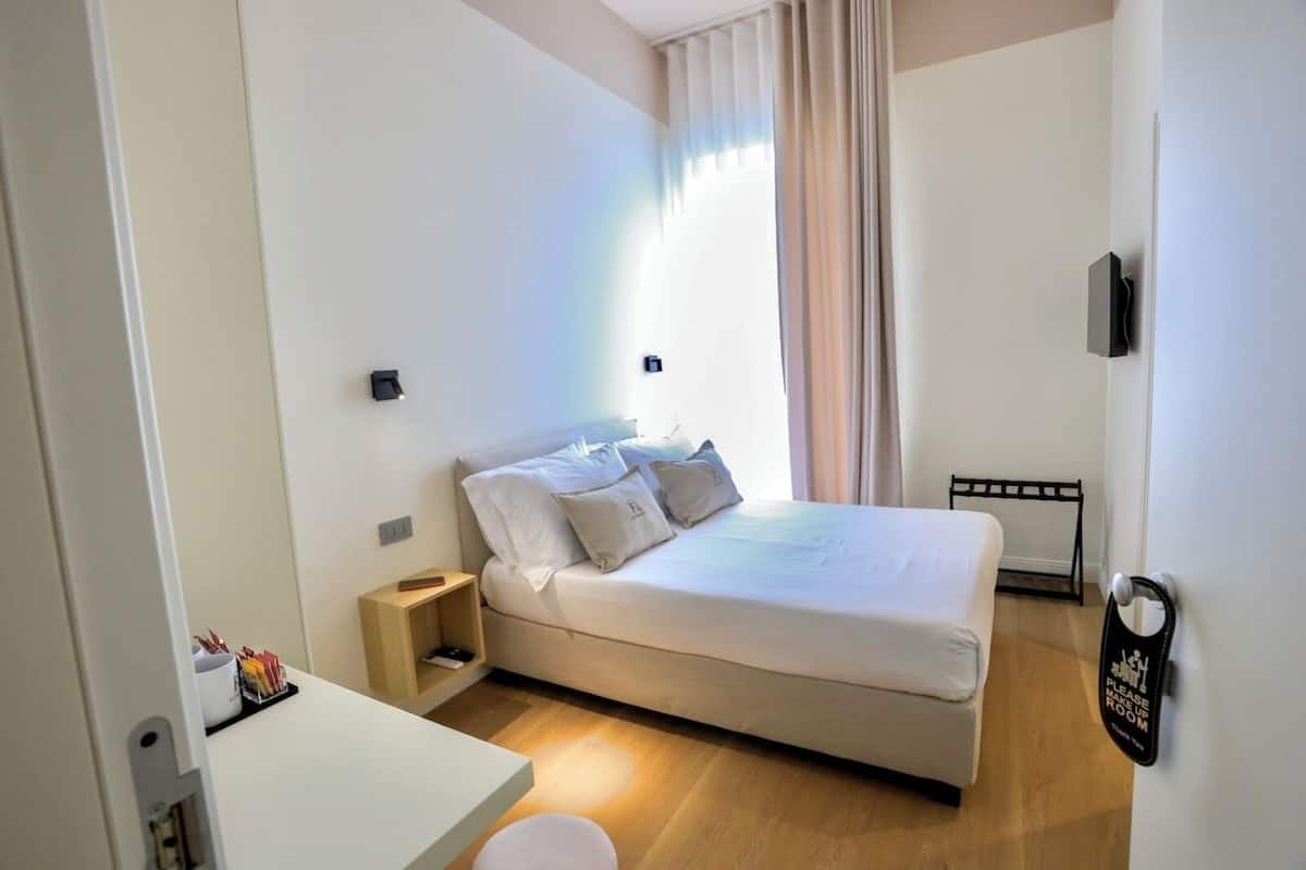 Una habitación de hotel con cama, mesita de noche y televisor montado en la pared.