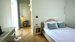 Hotellihuone, jossa on sänky, työpöytä kannettavalla tietokoneella, tuoli ja yöpöytä, jossa on lamppu.