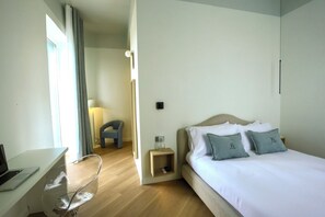 Quarto de hotel com cama, escrivaninha com laptop, cadeira e mesa de cabeceira com abajur.