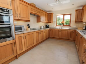 A kitchen with wooden cabinets, stainless steel appliances, a window with a view, and a tiled floor. - Yr Onnen (Rhayader)