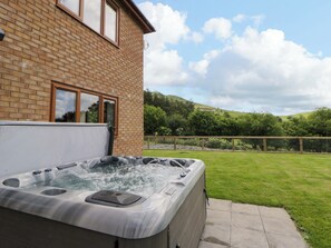 A hot tub outside a brick house with a grassy yard and hills in the background. - Yr Onnen (Rhayader)