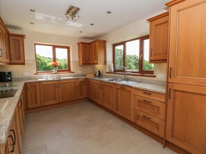 A kitchen with wooden cabinets, a granite countertop, a sink, and a window with a view of greenery. - Yr Onnen (Rhayader)