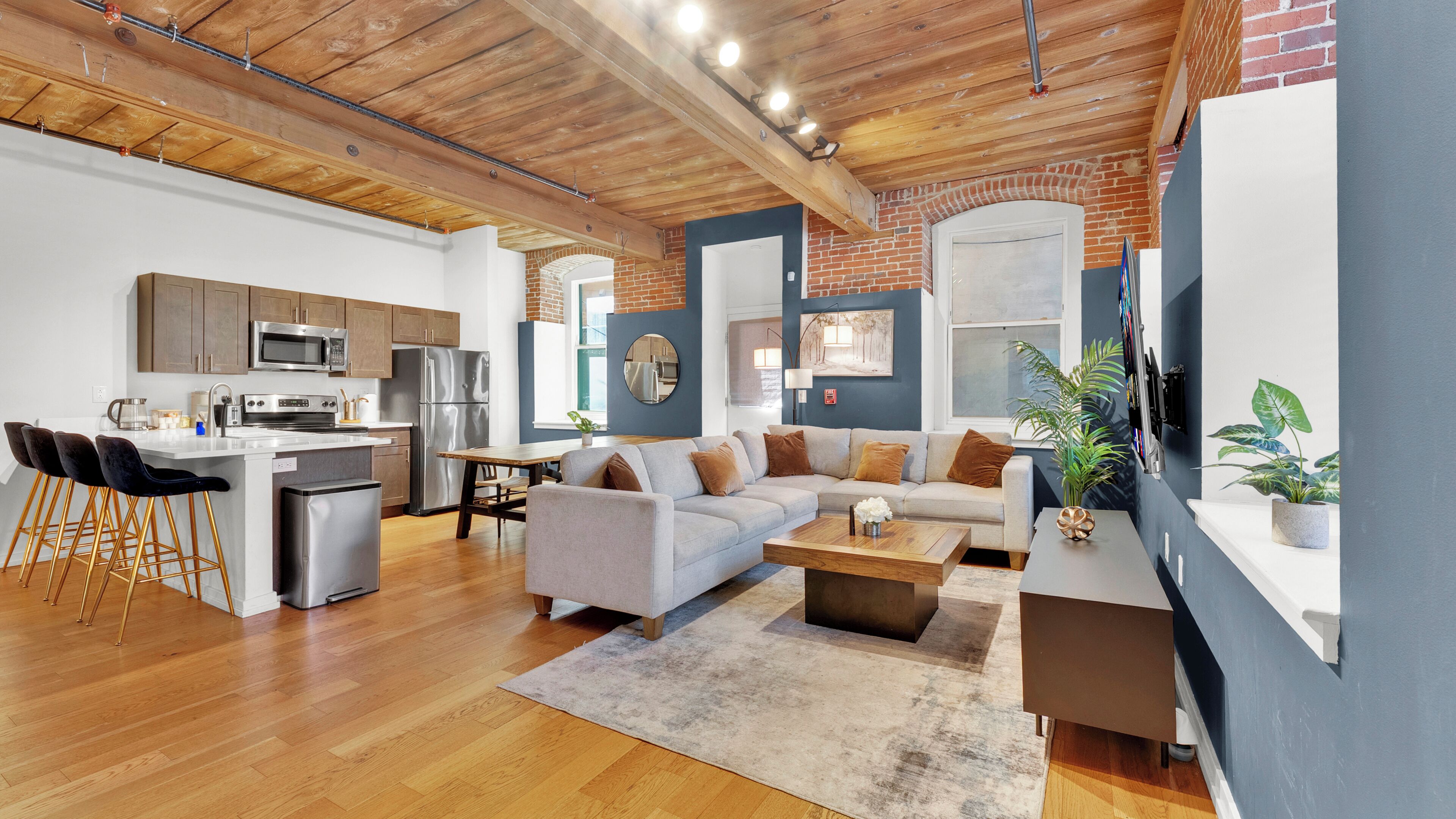 A modern kitchen with stainless steel appliances, a dining area with a sofa and coffee table, and a living room with a fireplace.