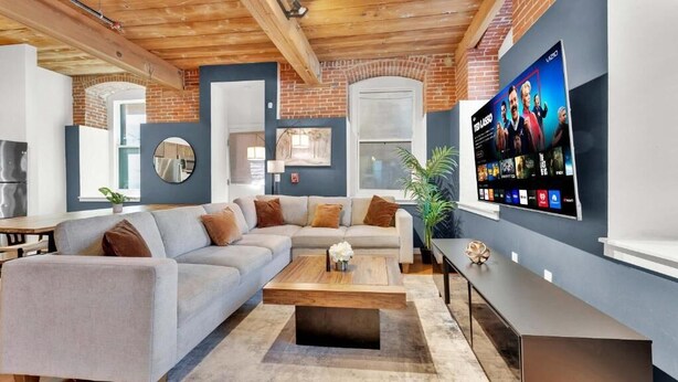 Ein modernes Wohnzimmer mit einem Ecksofa, einem Couchtisch, einem Flachbildfernseher und einer Ziegelwand.