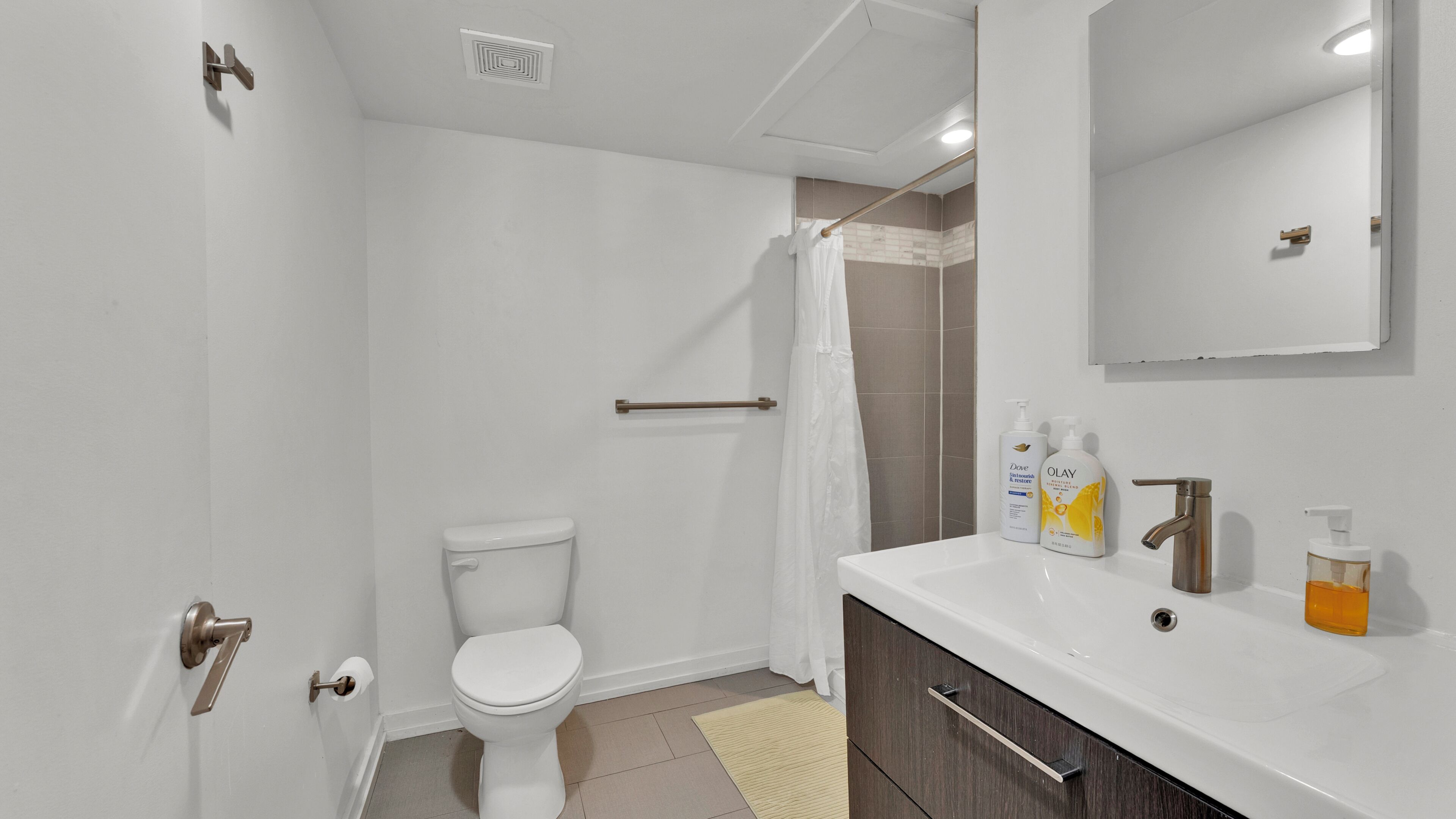 A bathroom with a toilet, shower, sink, and toiletries.