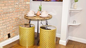 A room with a brick wall, a wooden table with cups and saucers, two yellow patterned trash bins, and a shelf with a plant. - New York Style Stay near Central Park (New York)