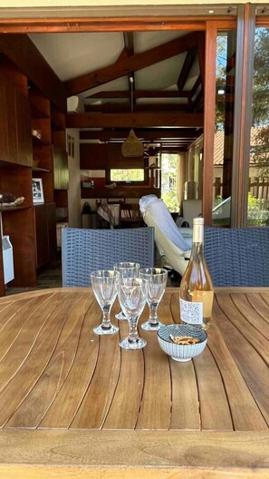 Ein Holztisch mit Weingläsern und einer Flasche, ein Korbstuhl und Blick ins Freie.