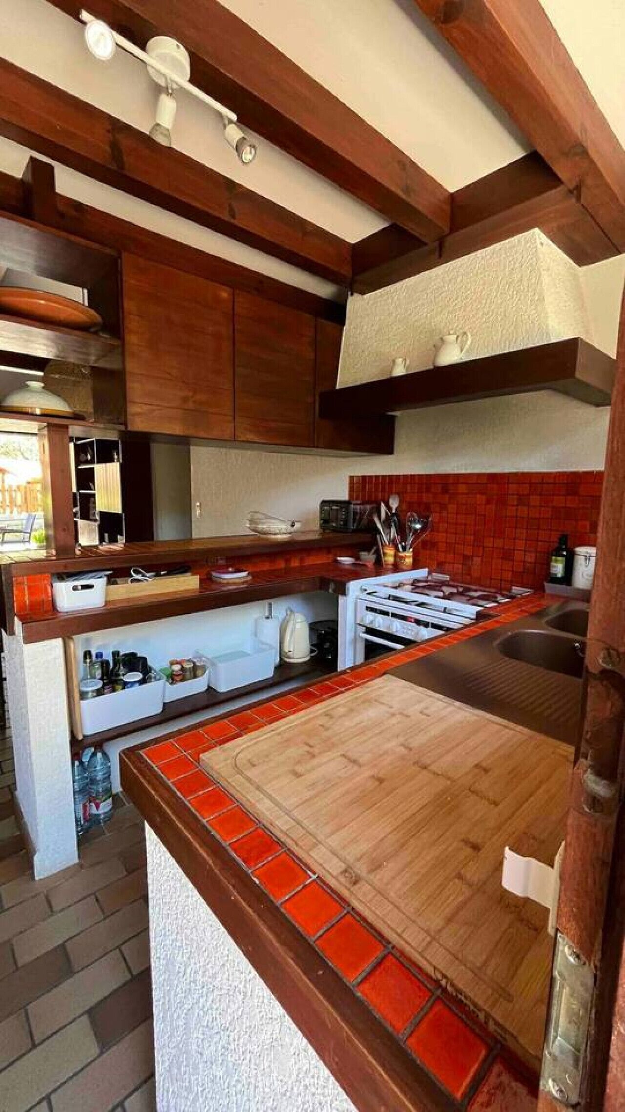 A kitchen with wooden cabinets, a red-tiled backsplash, a wooden countertop, and a built-in stove.