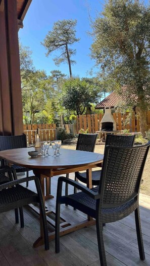 Eine Terrasse im Freien mit einem runden Tisch und Stühlen, einem Holzzaun und einem Grill im Hintergrund.