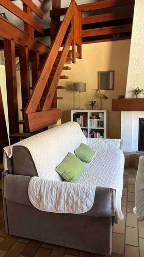 Ein gemütliches Zimmer mit einer Holztreppe, einem Sofa mit einer Decke, einem Bücherregal und einem Kamin.