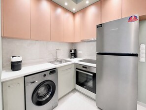 Een kleine keuken met een wasmachine, een koelkast en een koffiezetapparaat.