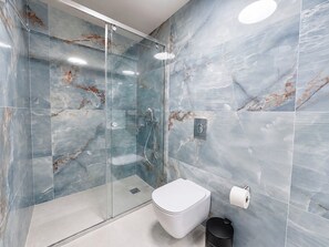 Een moderne badkamer met een douchecabine van glas, een wit toilet en een wand betegeld met marmer.