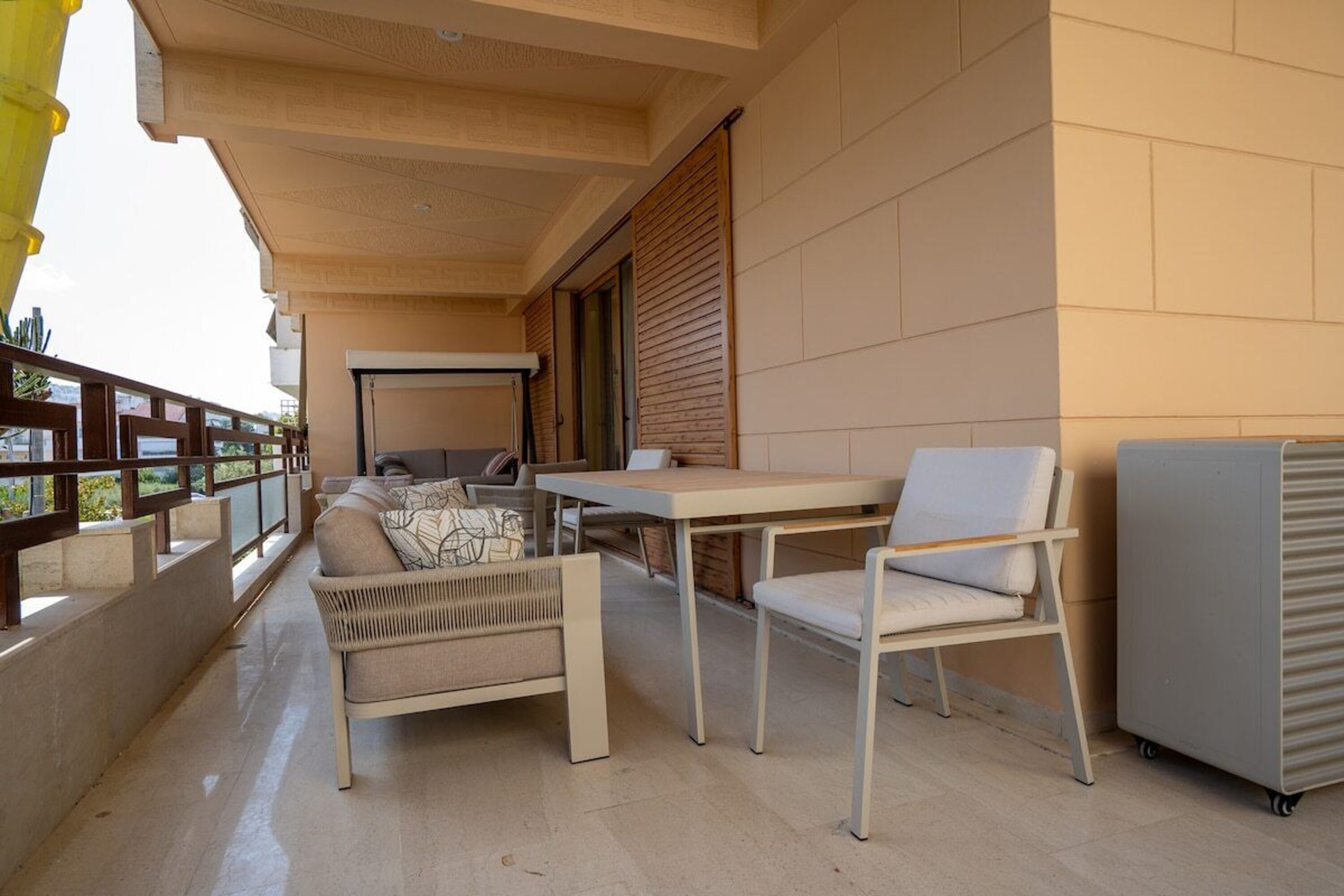 A balcony with a sofa, chairs, a table, and a refrigerator.