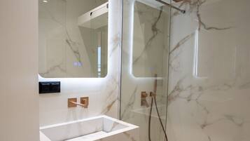 Un baño moderno con ducha envuelta en vidrio, paredes de mármol y lavamanos integrado.
