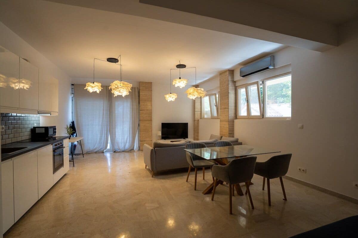 A modern kitchen with a dining area, a TV, and a large window.