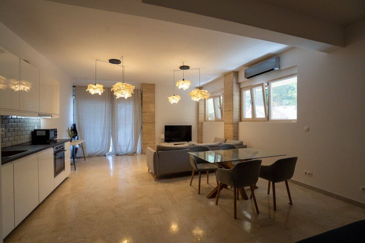 A modern kitchen with a dining area, a TV, and a large window.