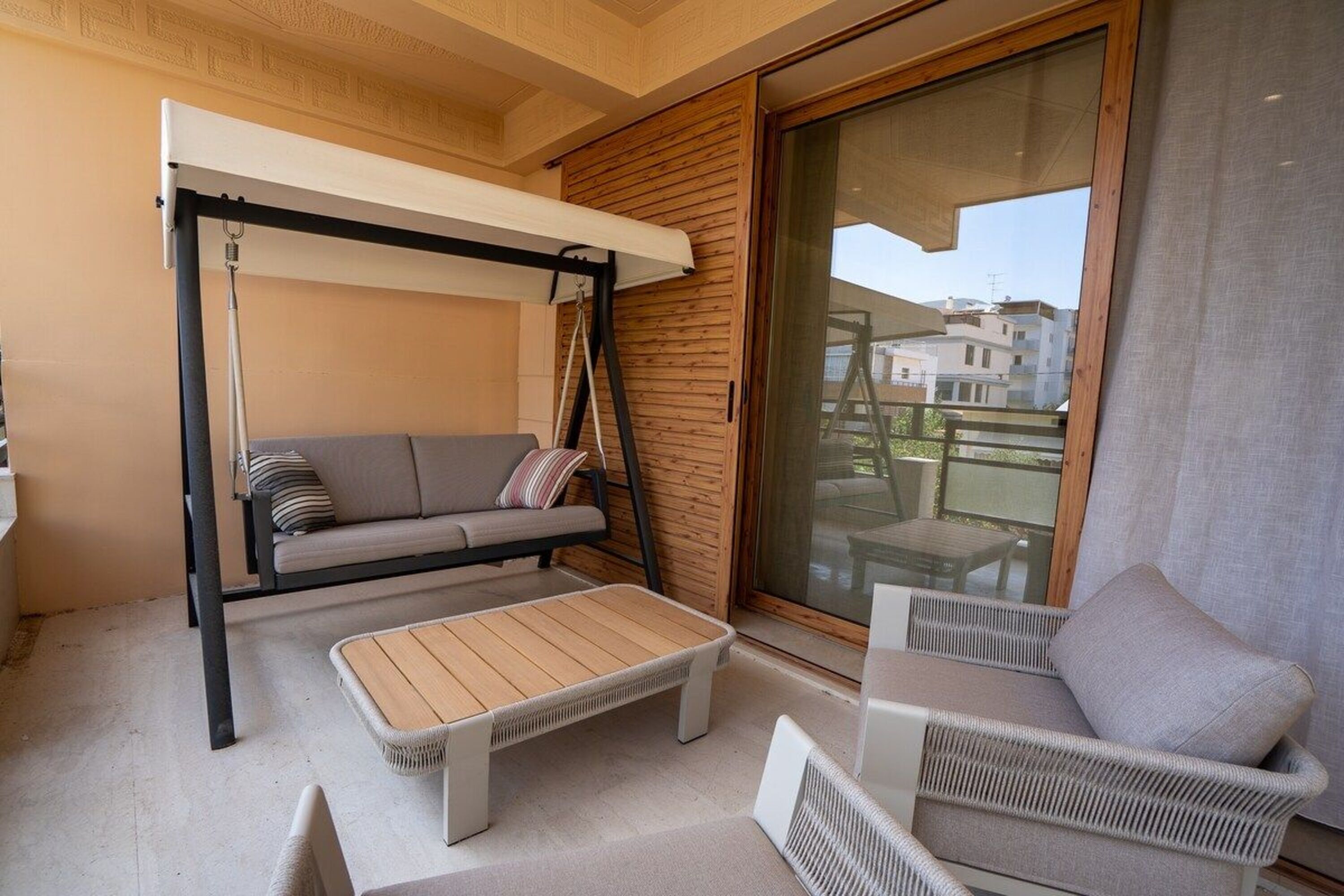A balcony with a sofa, a swing, a table, and wicker chairs.