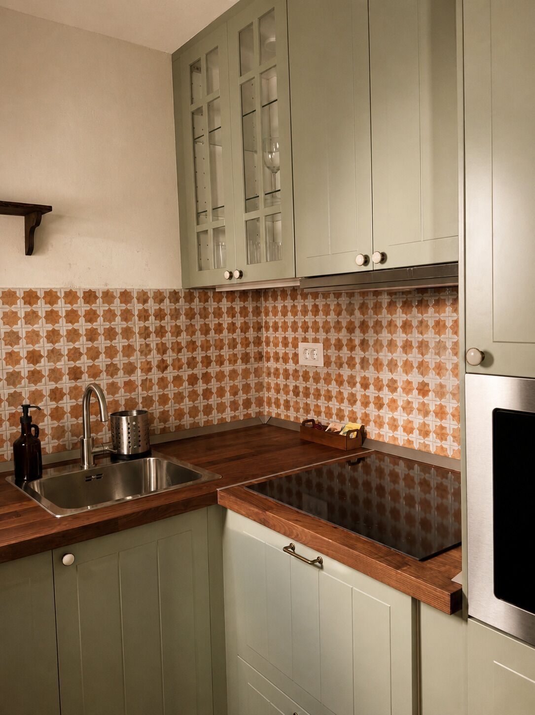 A kitchen with green cabinets, a stainless steel sink, and patterned backsplash.