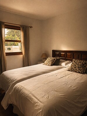 A room with two beds, a window with curtains, a nightstand with a lamp, and a wooden headboard. - La Piavera (Apartment with Private Garden) (La Laguna)
