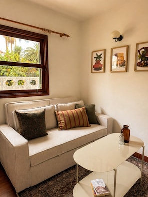 Ein Wohnzimmer mit einer Couch, einem Couchtisch, einem Fenster mit Blick auf Grünflächen und drei gerahmten Bildern an der Wand.