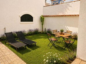 Eine Terrasse mit Tisch und Stühlen, ein kleines Fenster und eine Kakteenpflanze.