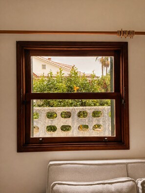 Ein Fenster mit Holzrahmen und Blick auf ein Gebäude und Grün.