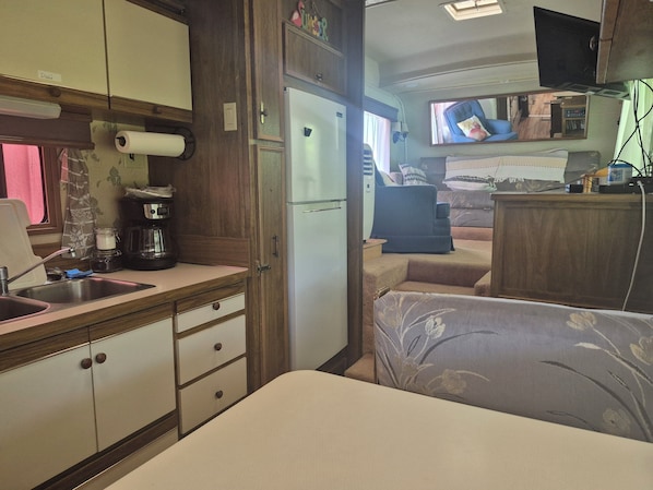 A compact RV interior with a kitchenette, a bed, and a television.