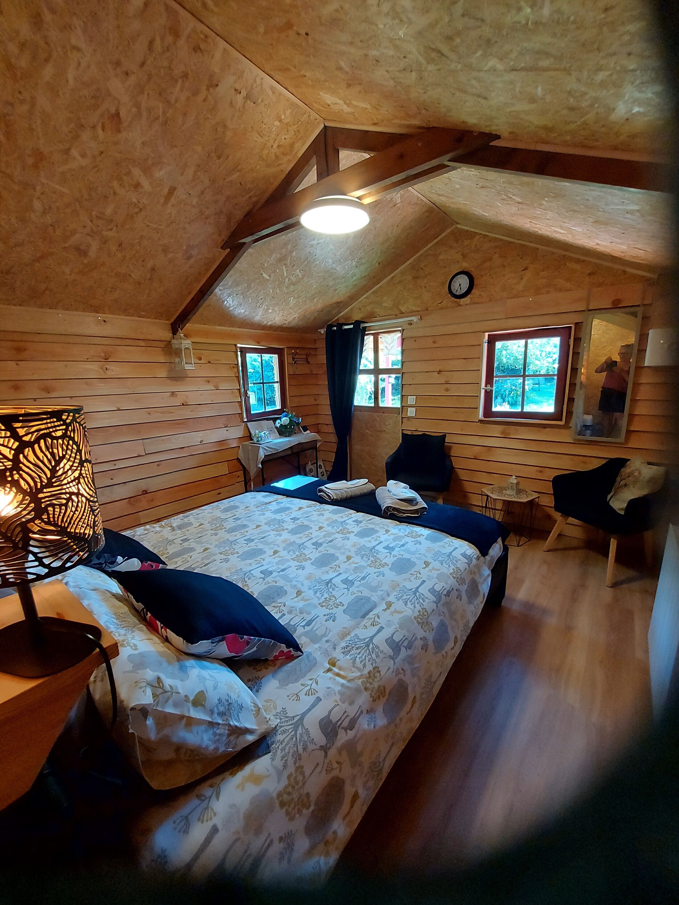 Un dormitorio acogedor en el ático, con cama, una mesa, una silla y un ventanal.