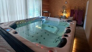 A spa room with a hot tub, wooden ceiling, and a window with blinds.