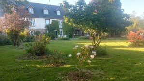 A residential property with a well-maintained lawn, a variety of flowering plants, and a large house with multiple windows and a chimney.