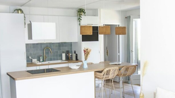 Una cocina moderna con armarios blancos, una isla de madera y un comedor con sillas de mimbre.