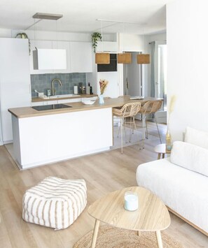 Una cocina moderna con armarios blancos, una isla de madera y un comedor con sillas de mimbre.