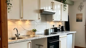 Ett modernt kök med vita skåp, en diskho i rostfritt stål, en inbyggd ugn och en kaffebryggare.