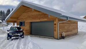 Una cabaña de madera con un garaje, un coche aparcado delante y un paisaje nevado.
