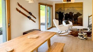 Un interior moderno con vigas de madera, una mesa de comedor con bancos, una silla blanca y un cuadro de vacas.